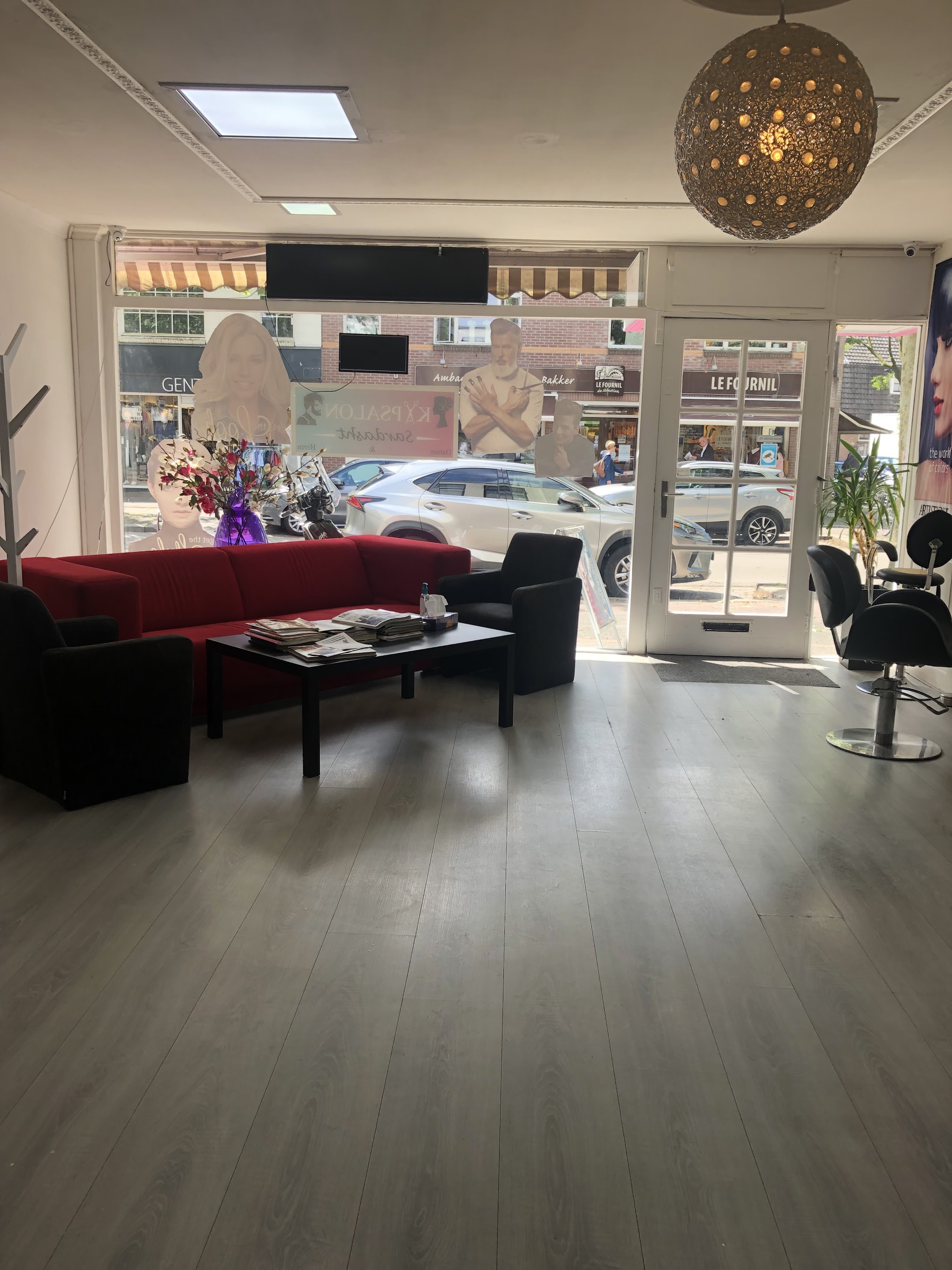 De salon van binnen: kappersstoelen, een zithoek met rode bank en de deur naar de straat